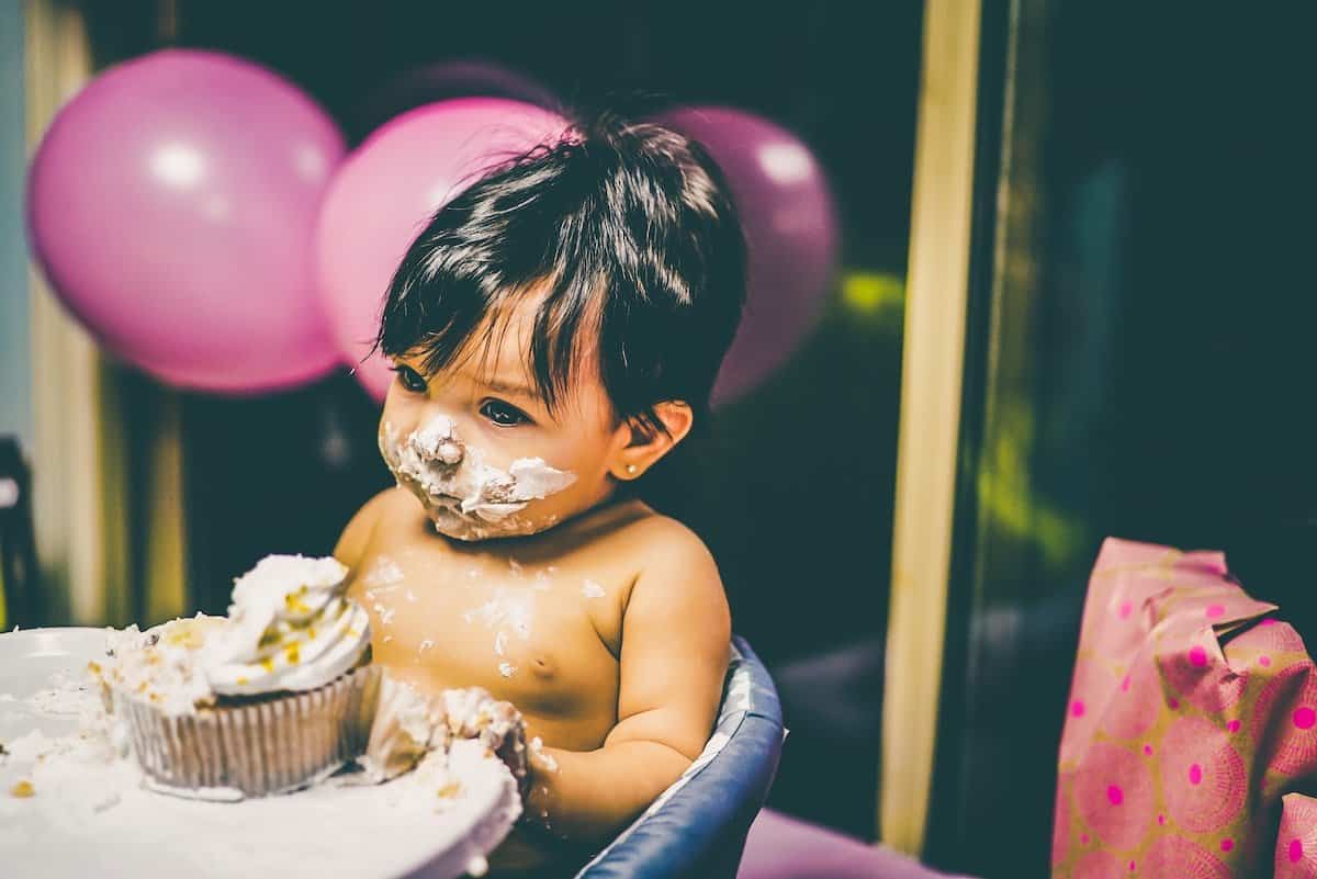 baby with black hair sitting in front of a cupcake with pink balloons in background